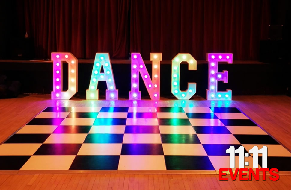 Light up DANCE letters 4ft high with multicoloured bulbs on fairground style chase pattern setup up behind a black and white chequered dance floor in osmington