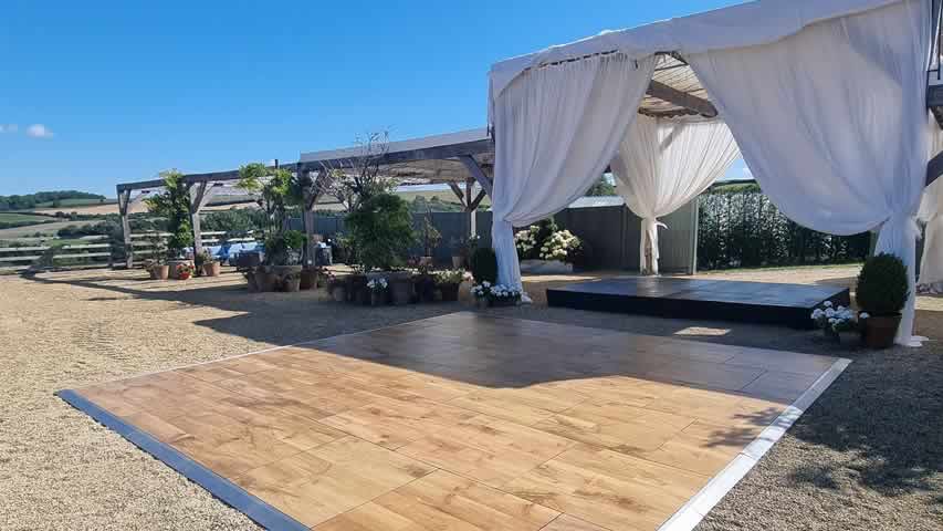A Cheddington Weddings Outdoor setup with Oak effect dance floor and black stage set for a band in Dorset